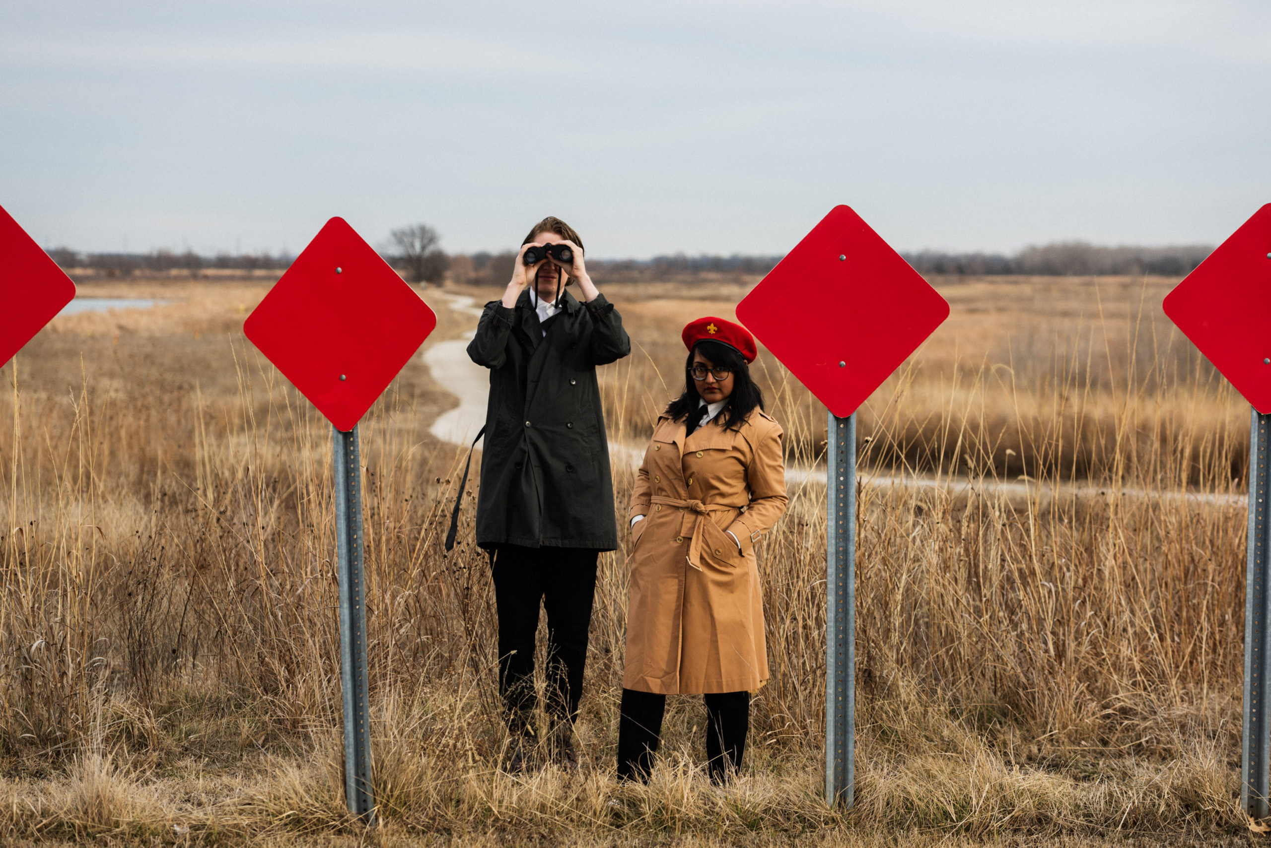 The duo of Sweeping Promises stand between red, diamond shaped road signs in front of a prairie of brown long grass